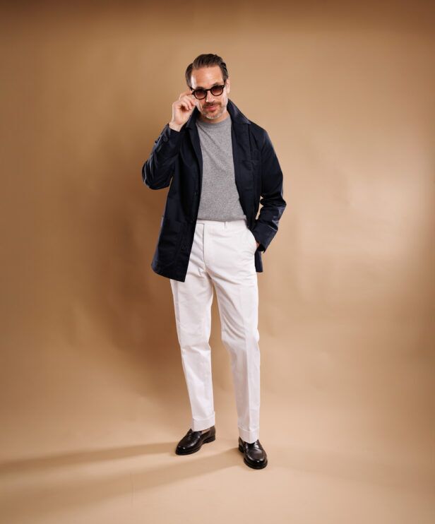 Man wearing black penny loafers with navy chore coat and white trousers in elevated casual outfit