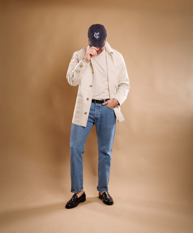 Preppy outfit featuring black penny loafers with light wash jeans and ivory canvas chore coat