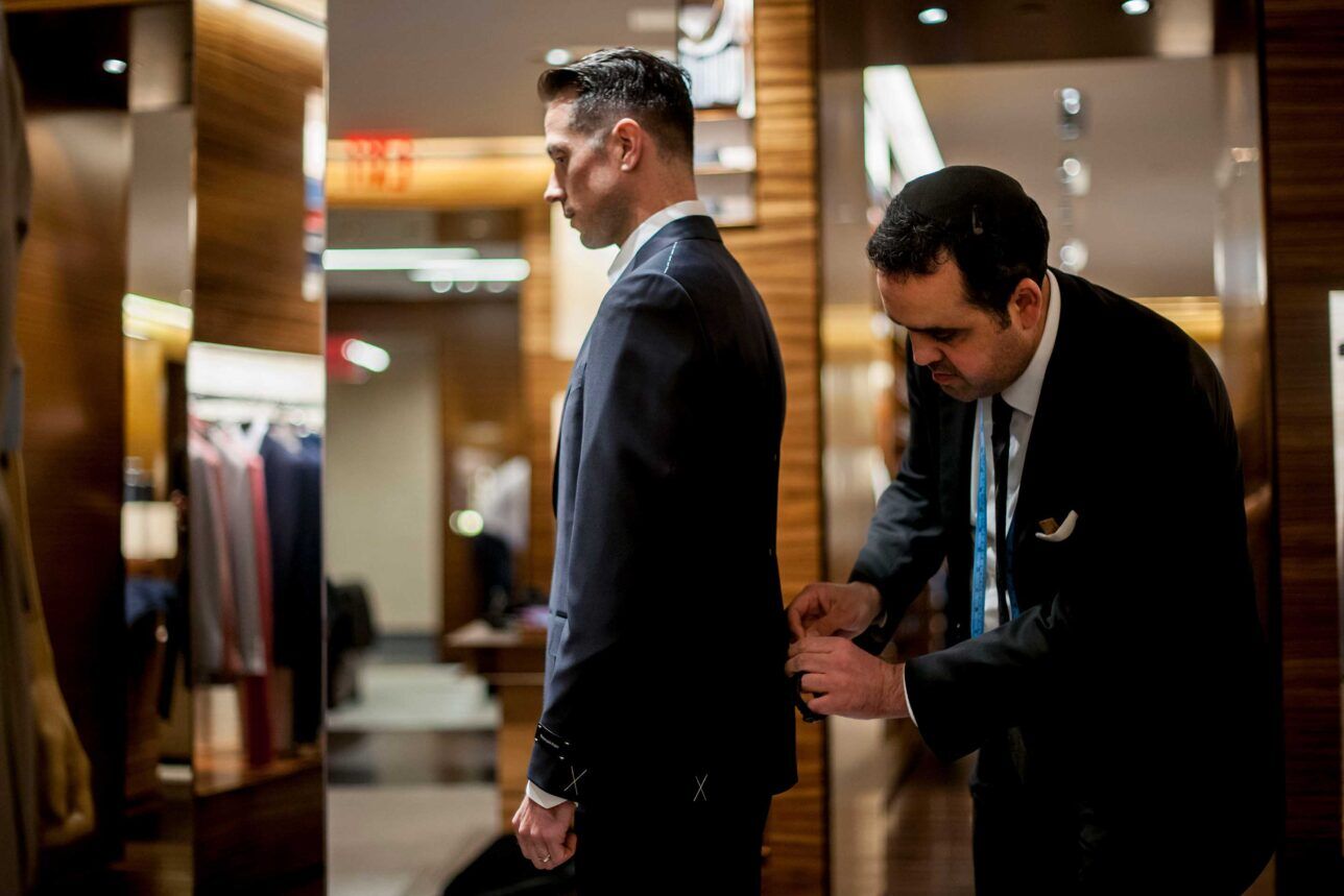 A tailor makes adjustments to a wedding suit jacket