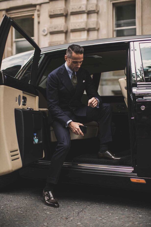 A confident man in a suit gets out of a Rolls Royce