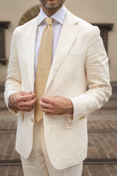 A cream linen suit styled with a white shirt and tan linen tie