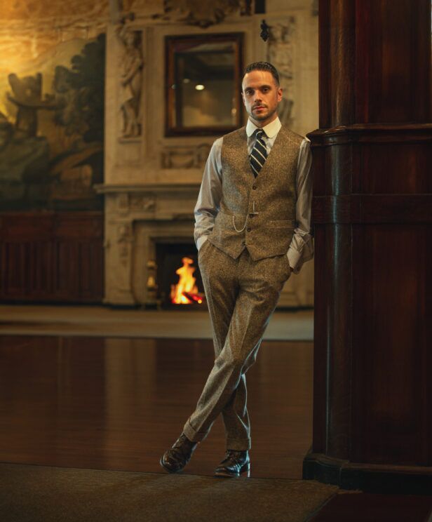 Olive brown donegal tweed waistcoat and trousers with a striped shirt and tie, by a fireplace