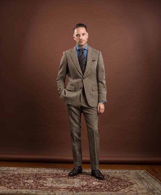 Brown donegal tweed suit with denim shirt, striped tie and brown loafers, worn by a model