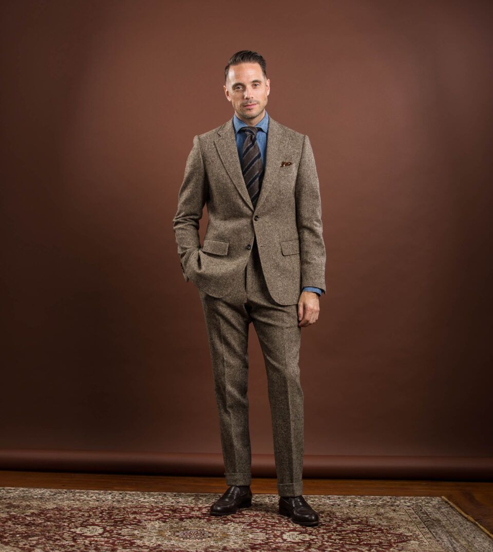 Brown donegal tweed suit with denim shirt, striped tie and brown loafers, worn by a model
