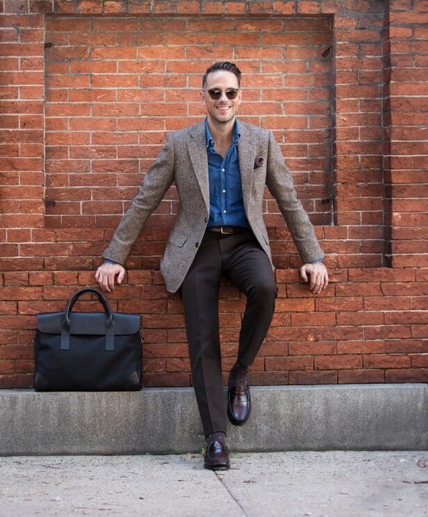 Brown donegal tweed sport coat with denim shirt, dark brown trousers and penny loafers, worn by a model against a brick wall