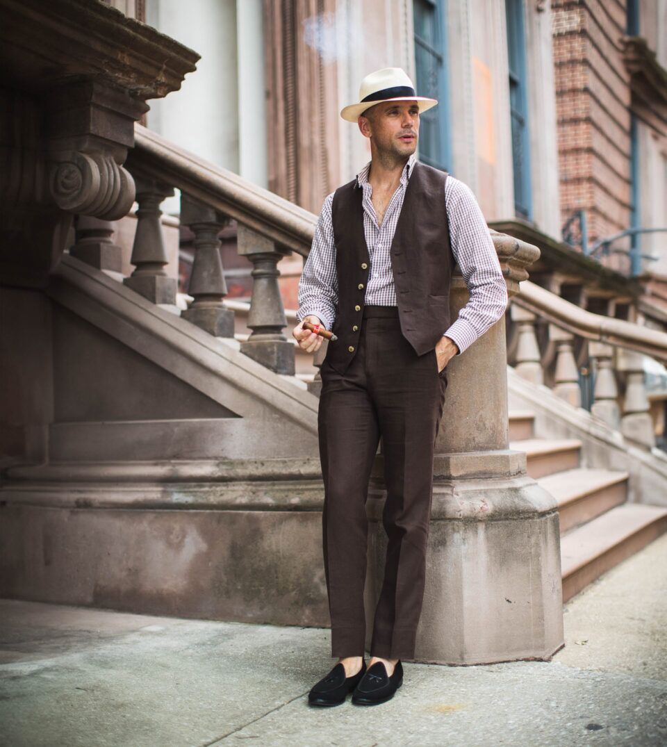 Brown linen waistcoat and matching trousers with gingham shirt, panama hat and black loafers, worn by a model on a stoop