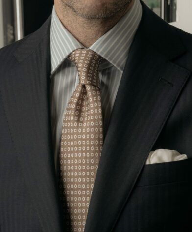 Navy herringbone suit jacket with blue striped shirt, tan medallion silk tie and white pocket square, worn by a model