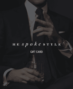 Navy suit with a white shirt and navy knit tie, on a dimmed He Spoke Style gift card