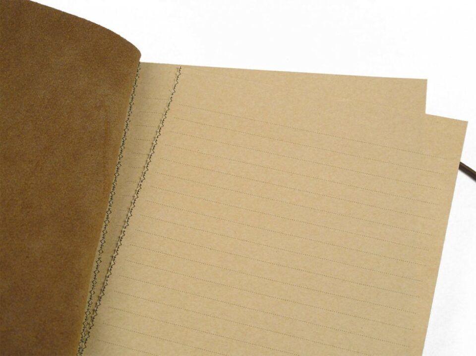 Tan leather notebook open to stitched kraft paper pages with ruled lines, a close-up detail