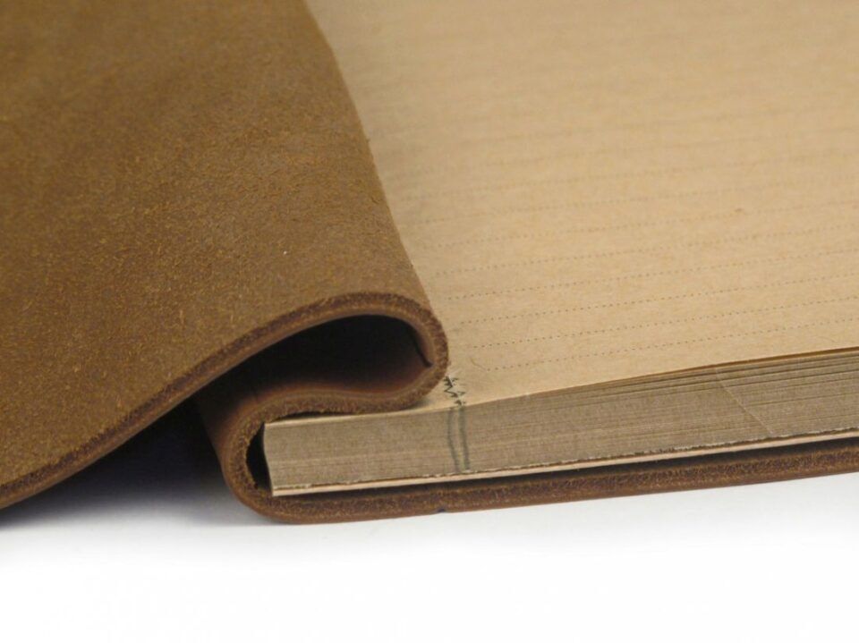 Tan leather notebook cover with stitched kraft paper pages, a close-up of the spine