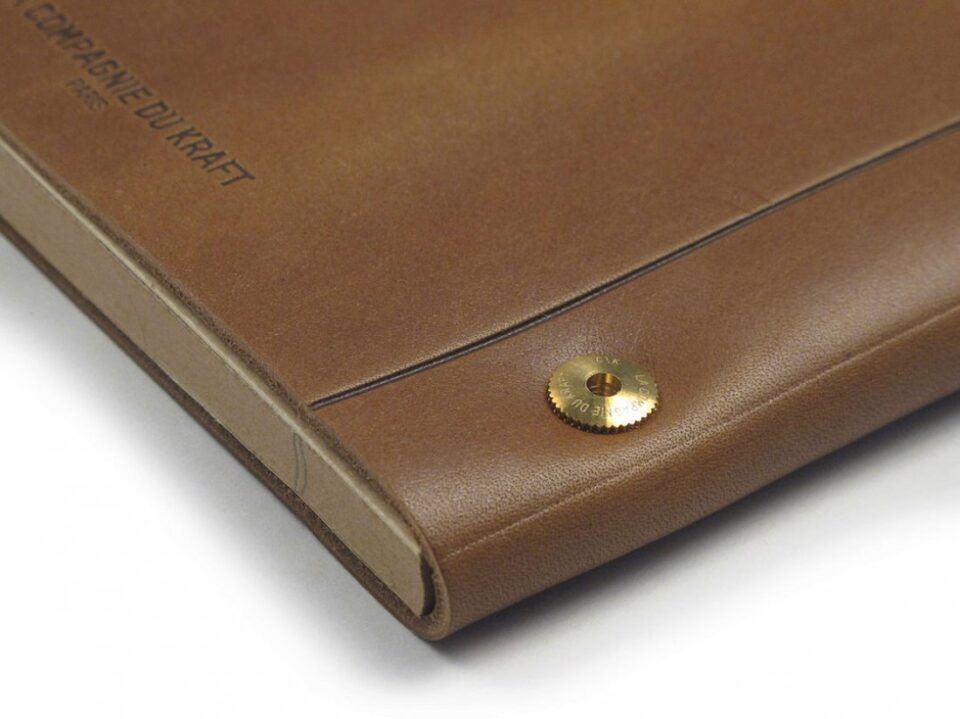 Tan leather notebook cover with embossed lettering and brass screw stud, a close-up detail of the corner