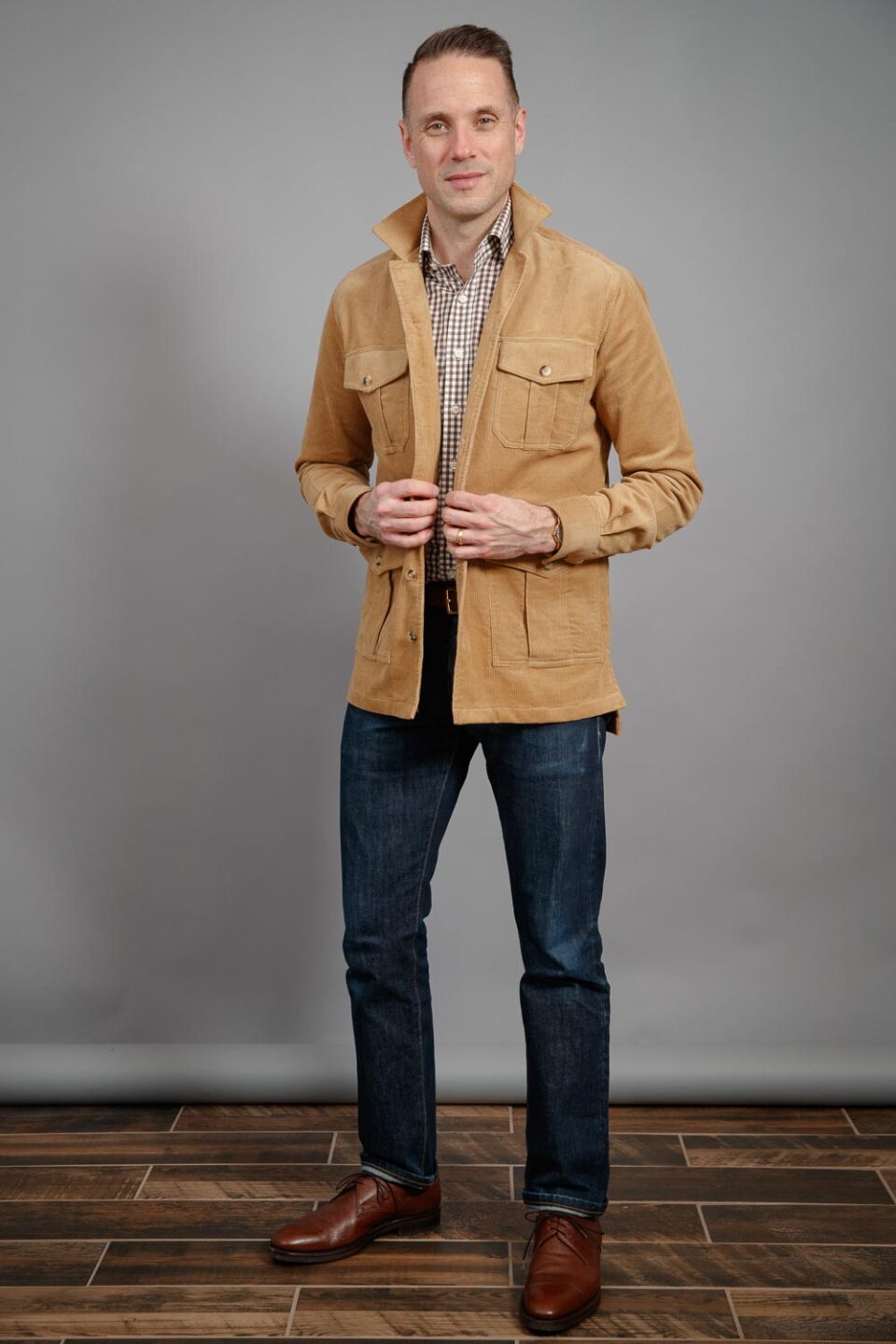 Tan corduroy four-pocket field jacket with brown check shirt and dark denim jeans, worn by a model