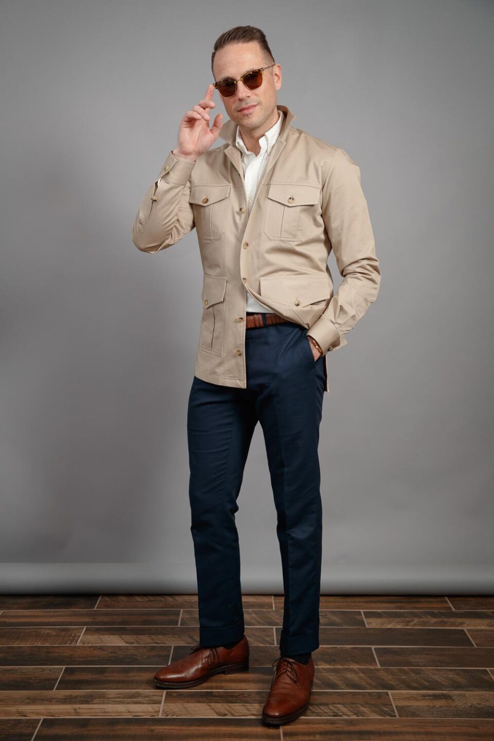 Khaki cotton safari jacket with four patch pockets, white polo and navy trousers, worn by a model