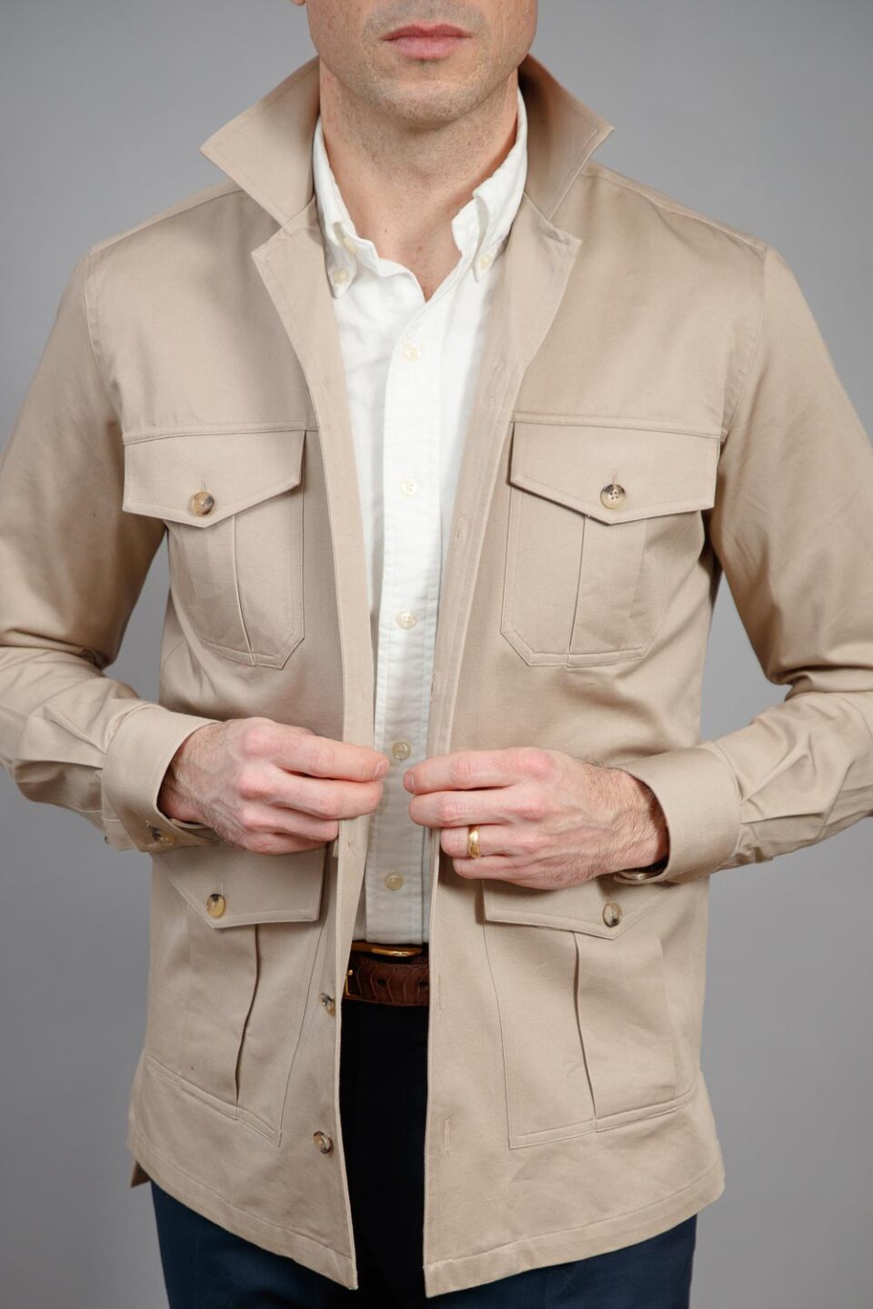 Tan cotton four-pocket safari jacket with stand collar, worn open over a white shirt by a model