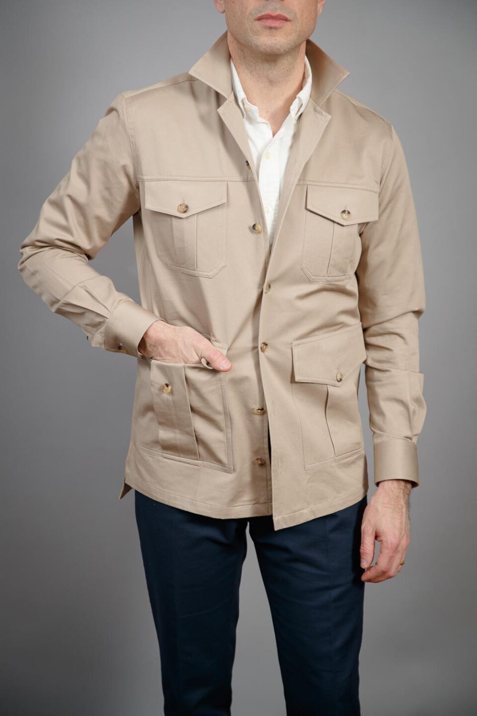 Tan cotton four-pocket safari shirt jacket with white shirt and navy trousers, worn by a model