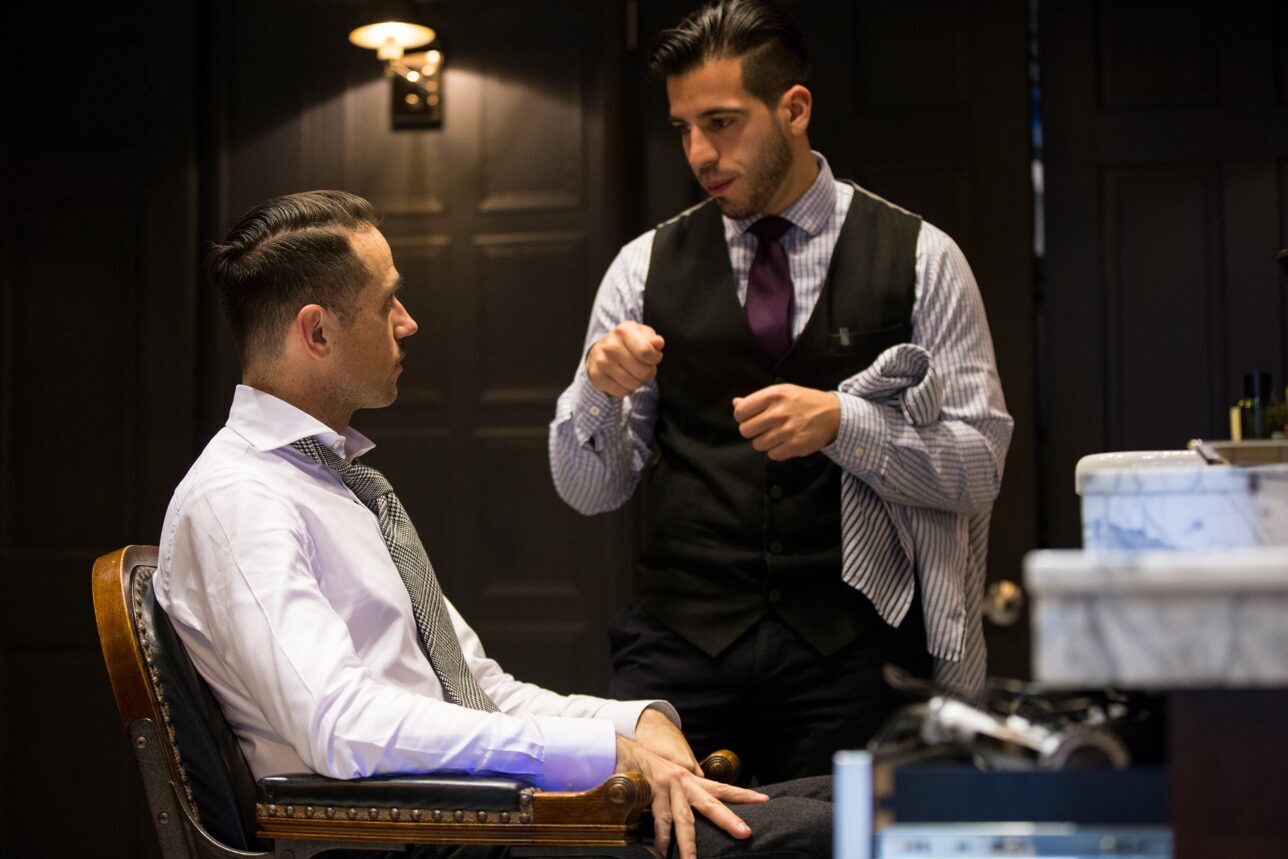 Black wool waistcoat with purple tie worn by a barber, with a seated client in a glen check tie