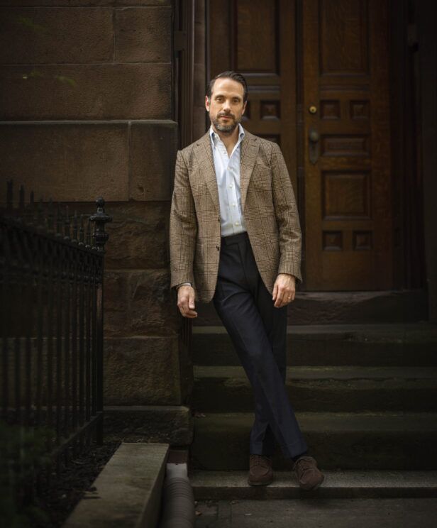 Brown glen plaid sport coat with light blue shirt and navy flannel trousers, on brownstone steps