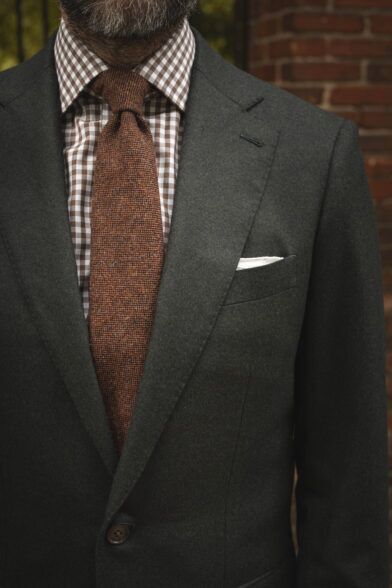 Forest green flannel suit jacket with brown gingham shirt, rust wool tie and white pocket square, worn by a model