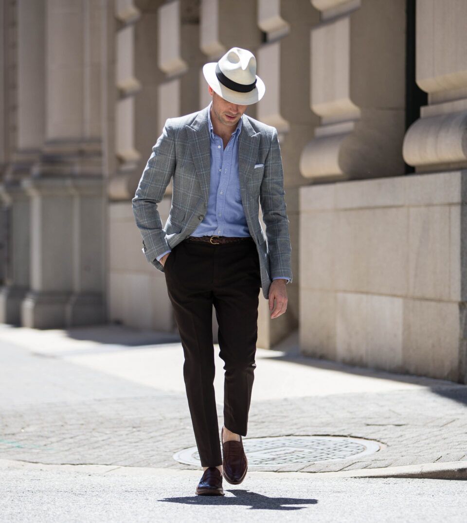 Grey windowpane plaid sport coat with blue oxford shirt, brown trousers and loafers, worn by a model on a city street