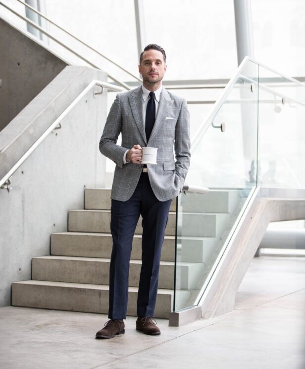 Grey windowpane flannel sport coat with navy knit tie, white shirt and navy trousers, worn by a model