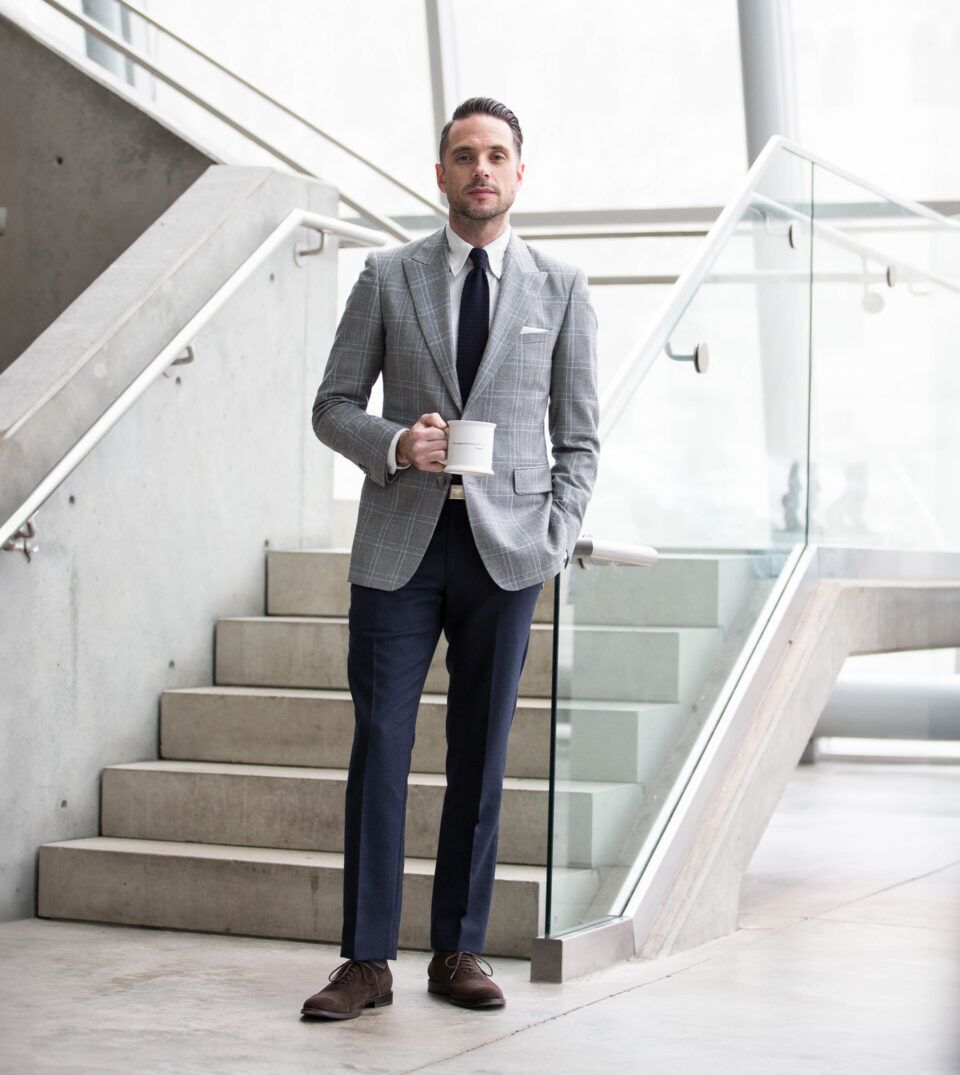 Grey windowpane flannel sport coat with navy knit tie, white shirt and navy trousers, worn by a model