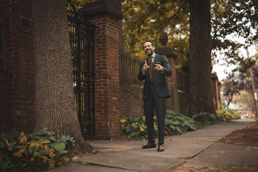 Forest green flannel suit with checked shirt, brown knit tie and brown brogues, worn by a model on a tree-lined sidewalk