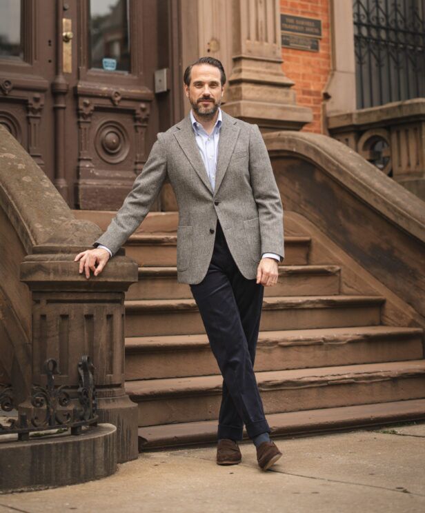 Grey herringbone tweed sport coat with blue shirt and navy corduroy trousers, on brownstone steps