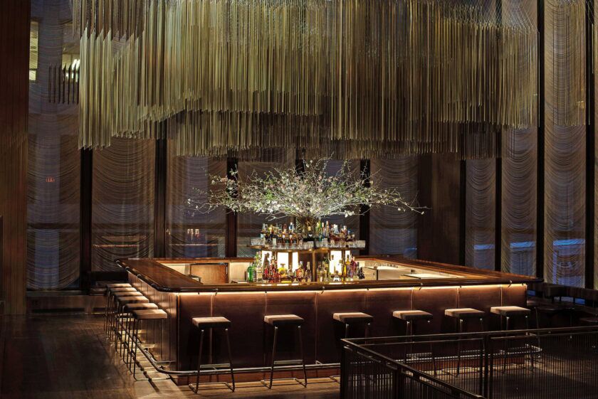 Wood and brass bar with leather stools and a sculptural metal ceiling in a midcentury dining room, a lifestyle scene