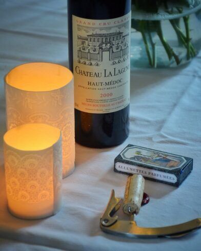 Bordeaux wine bottle with lit candles, matchbox and corkscrew on white linen, a styled lifestyle scene