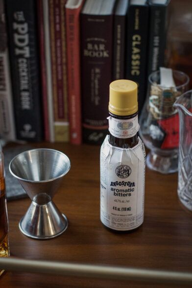 Angostura aromatic bitters bottle beside a stainless steel jigger on a wooden bar cart, a styled lifestyle scene