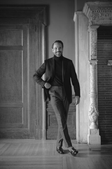 Black basketweave sport coat with dark turtleneck, pinstripe trousers and loafers, worn by a model in a styled interior