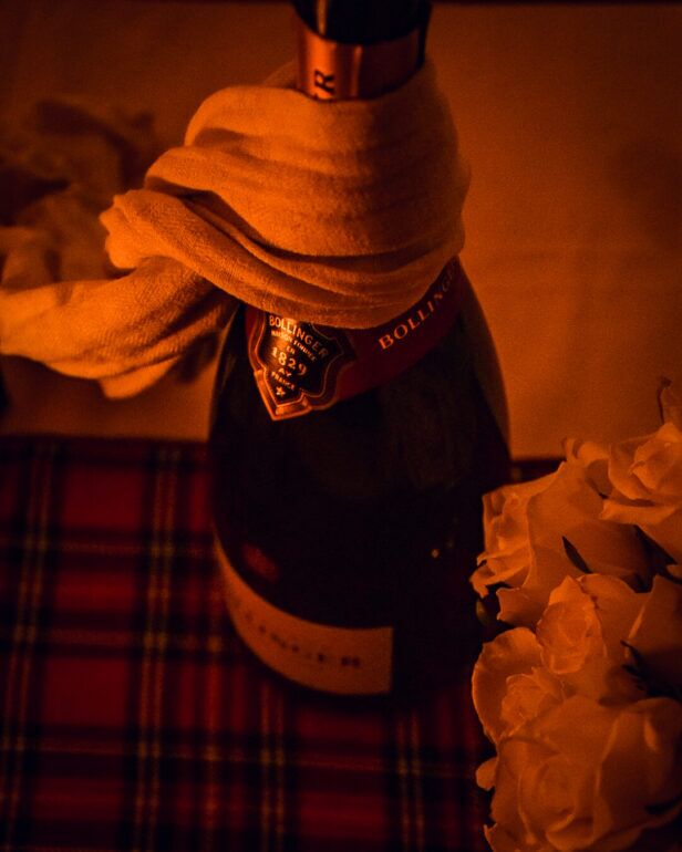 Red and white tartan cloth beneath a towel-wrapped champagne bottle and white roses, styled holiday scene