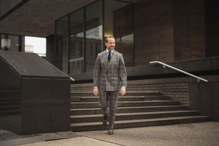 Grey plaid flannel double-breasted suit with blue shirt, navy tie and brown oxfords, worn by a model on city steps