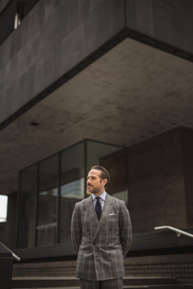Grey plaid flannel double-breasted suit with blue shirt, navy tie and white pocket square, worn by a model