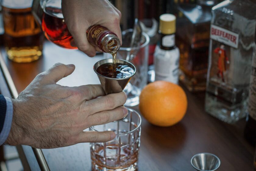 Bourbon poured into a steel jigger over a cut-glass tumbler at a home bar cart, a styled lifestyle scene