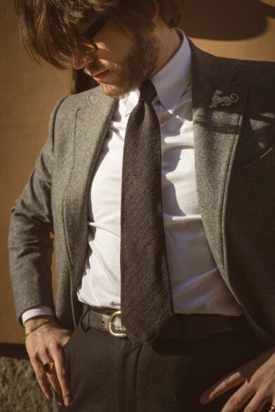 Grey flannel sport coat with white shirt, dark brown silk tie and leopard lapel pin, worn by a model