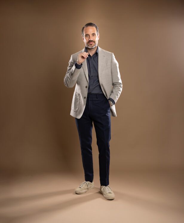 Light grey patch-pocket sport coat with navy denim shirt, navy trousers and taupe sneakers, worn by a model