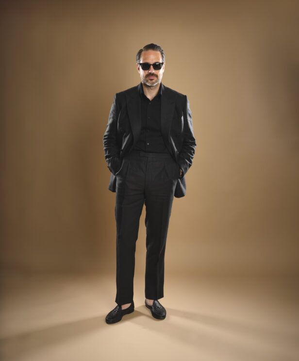Black linen double-breasted suit with peak lapels, black shirt and black tassel loafers, worn by a model