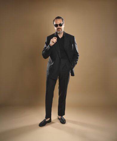 Black double-breasted linen suit with black shirt and black tassel loafers, worn by a model