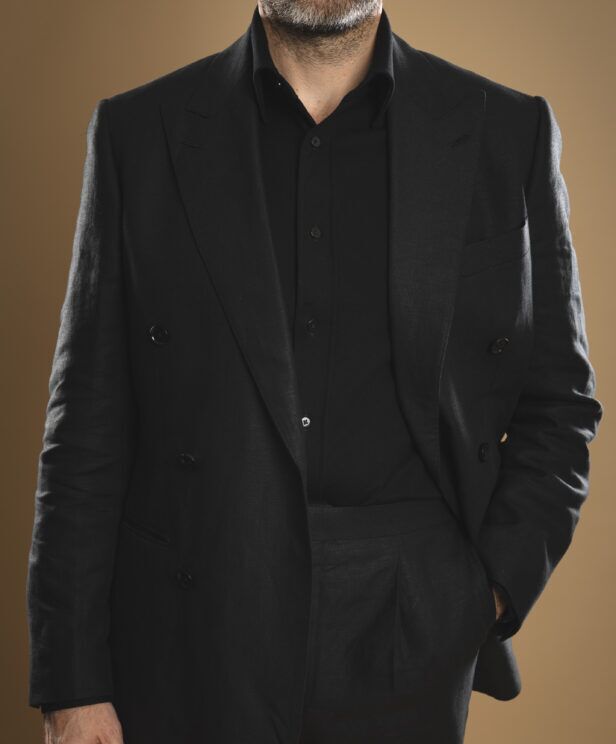 Black linen double-breasted suit with peak lapels, worn open over a black shirt by a model