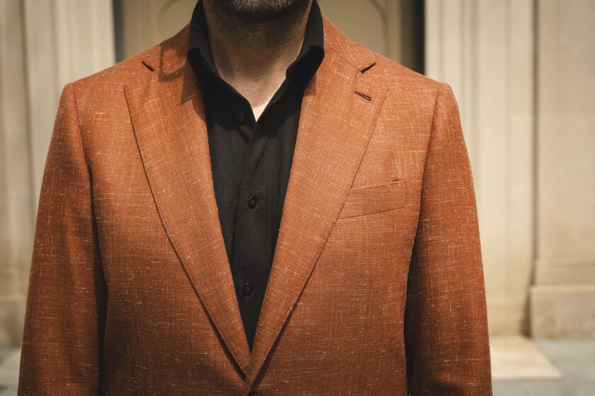 Terracotta textured sport coat with notch lapels over a black knit polo, a close-up of the chest and lapel