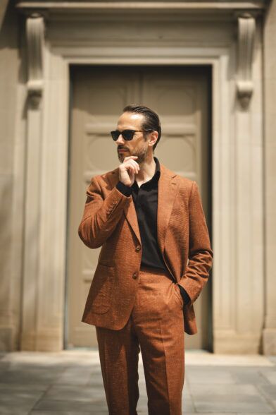 Terracotta textured linen-blend suit with black polo shirt and sunglasses, worn by a model outdoors