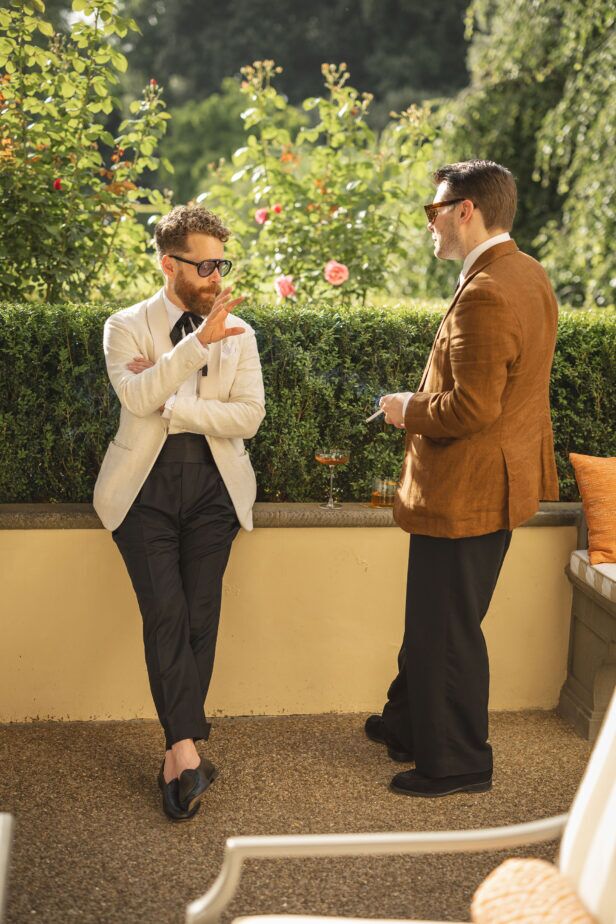 Cream shawl collar dinner jacket with black bow tie and trousers beside a tan linen sport coat, garden party scene
