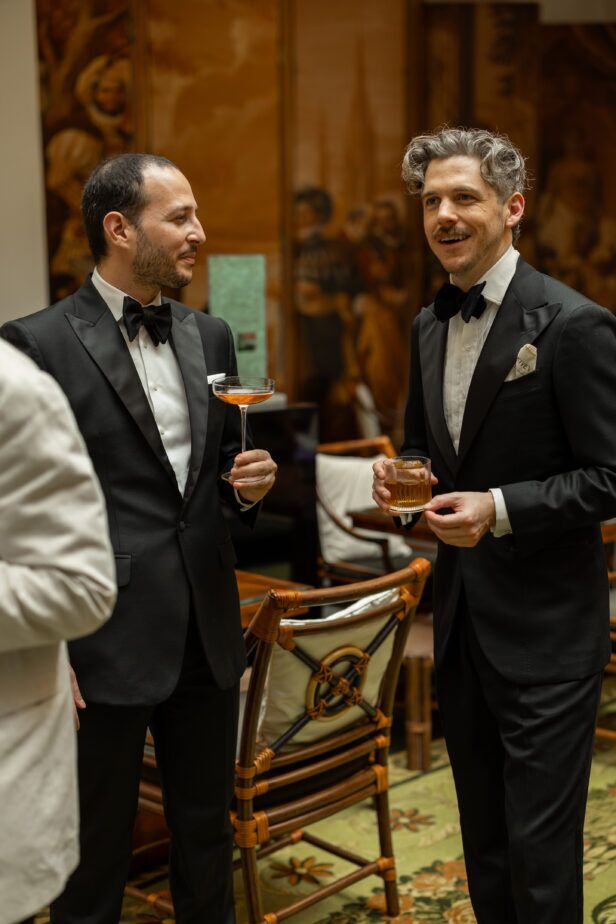 Black tuxedos with peak lapels, white dress shirts and black bow ties, worn by two men at a cocktail reception