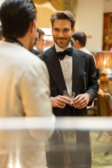 Black double-breasted peak lapel dinner jacket with pleated bib shirt and black bow tie, worn at a cocktail event