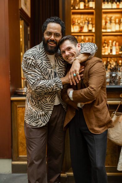 Zebra-print sport coat with brown trousers and a rust linen jacket with dark trousers, worn by two men at a bar