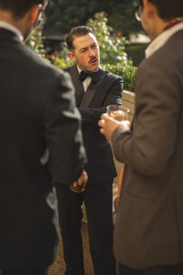 Black peak lapel dinner jacket with white shirt and black bow tie, worn at an outdoor cocktail gathering