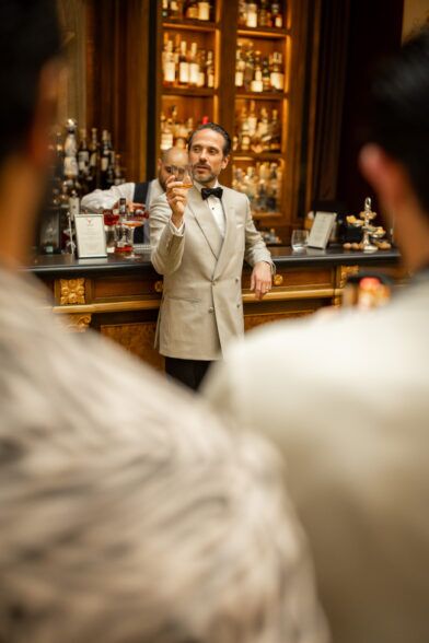 Ivory double-breasted shawl collar dinner jacket with black bow tie and trousers, worn at a bar in a styled event scene