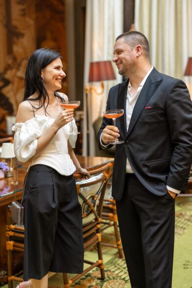 Black single-breasted suit with open white shirt and red pocket square, worn with cocktails in a hotel bar