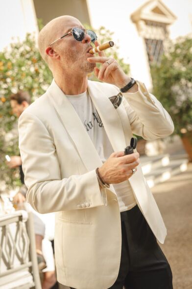 Ivory shawl collar dinner jacket with white tee and printed pocket square, worn by a man smoking a cigar
